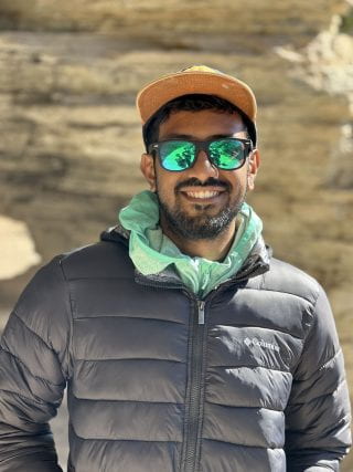 A portrait of Riasad in shades in front of geological feature